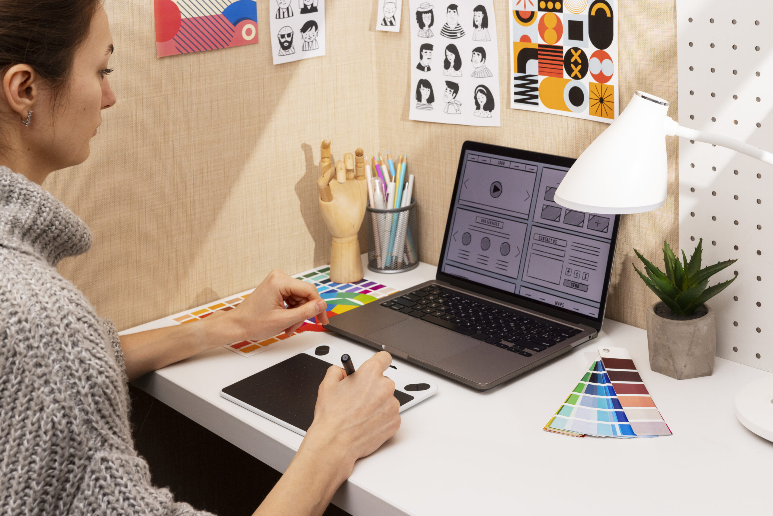 A designer's desk with a computer displaying graphic website wireframe and creative tools.