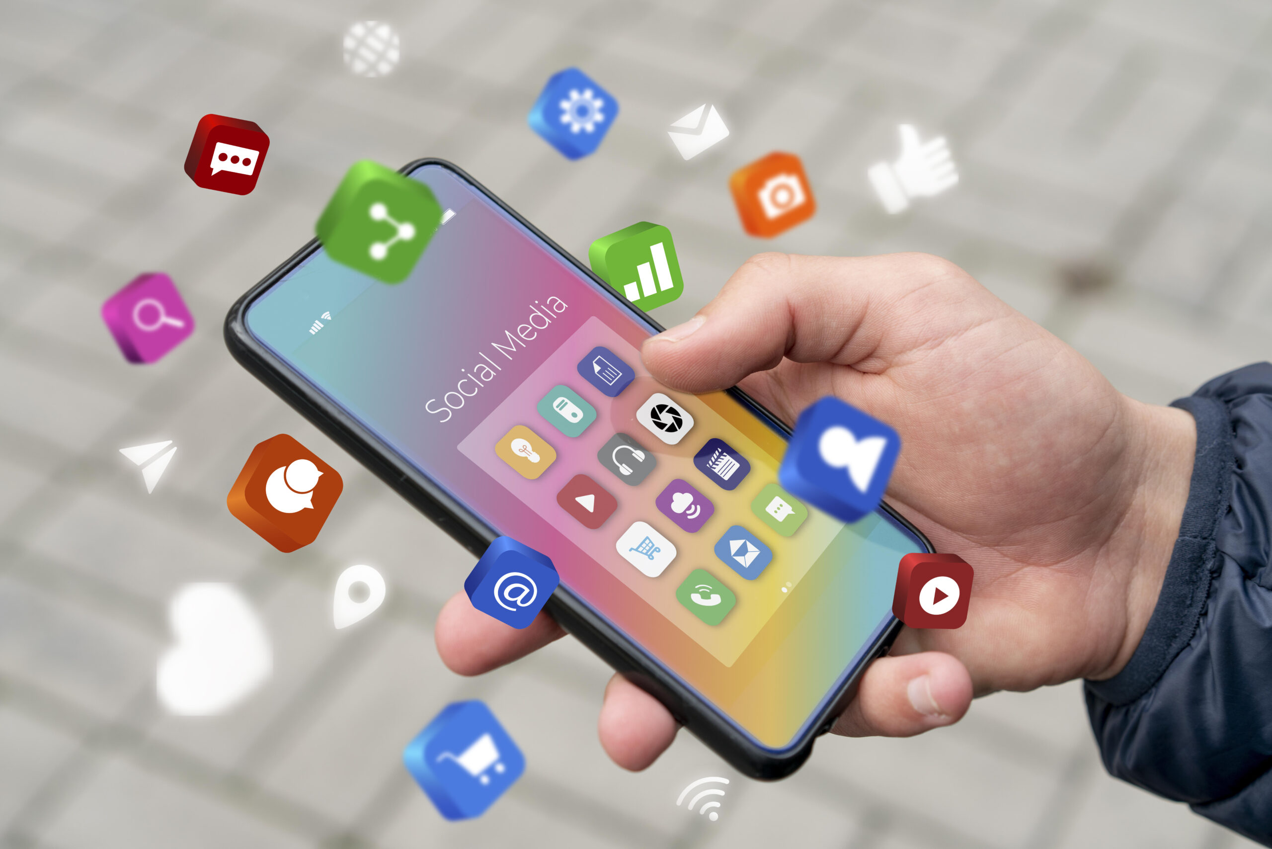Hand in a blue shirt holding a phone with social media icons, representing social media engagement.