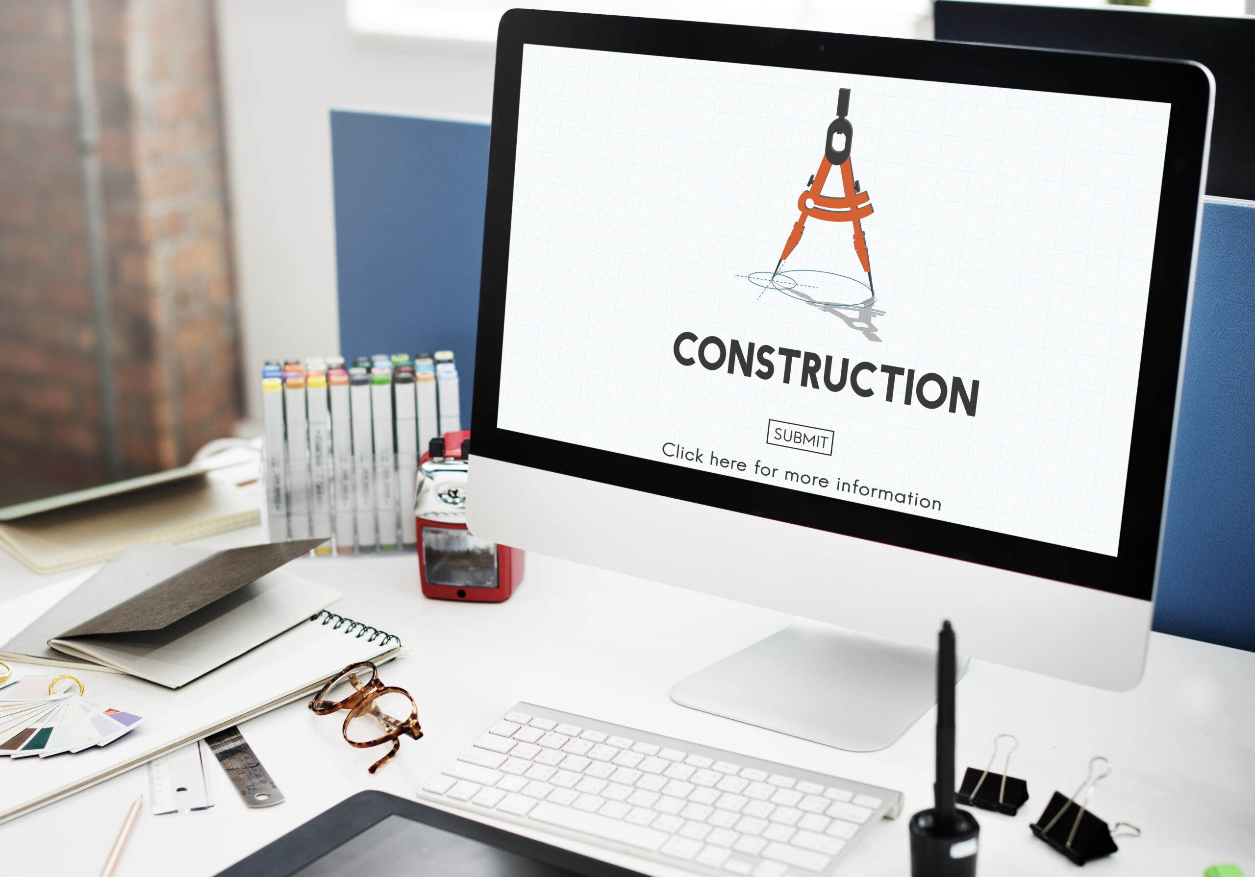 Construction architecture site concept shown on an iMac, with stationary, papers, and glasses on the table.