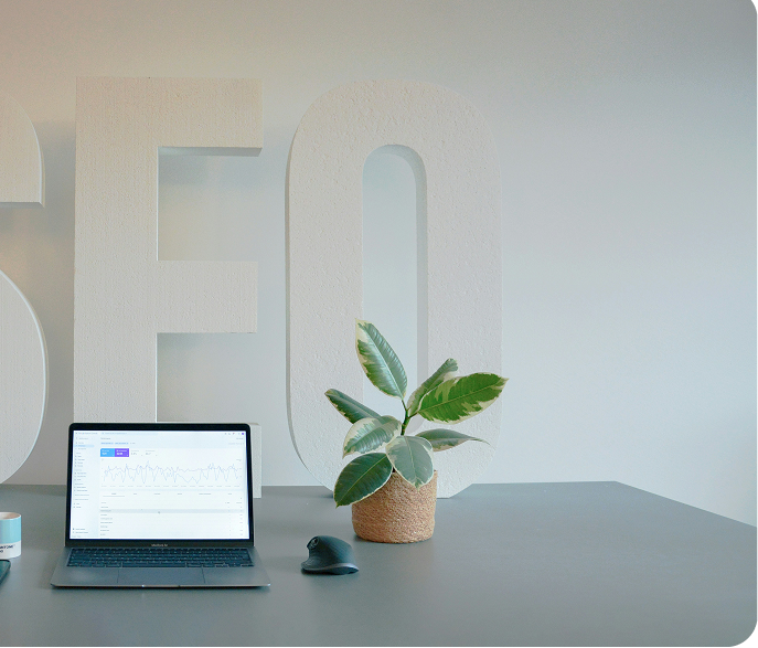 A well-lit desk setup in Johor Bahru, Malaysia, featuring SEO-related text on a background, a coffee mug, an iPad, a MacBook, and a small plant, but it appeared the image has been cropped half.